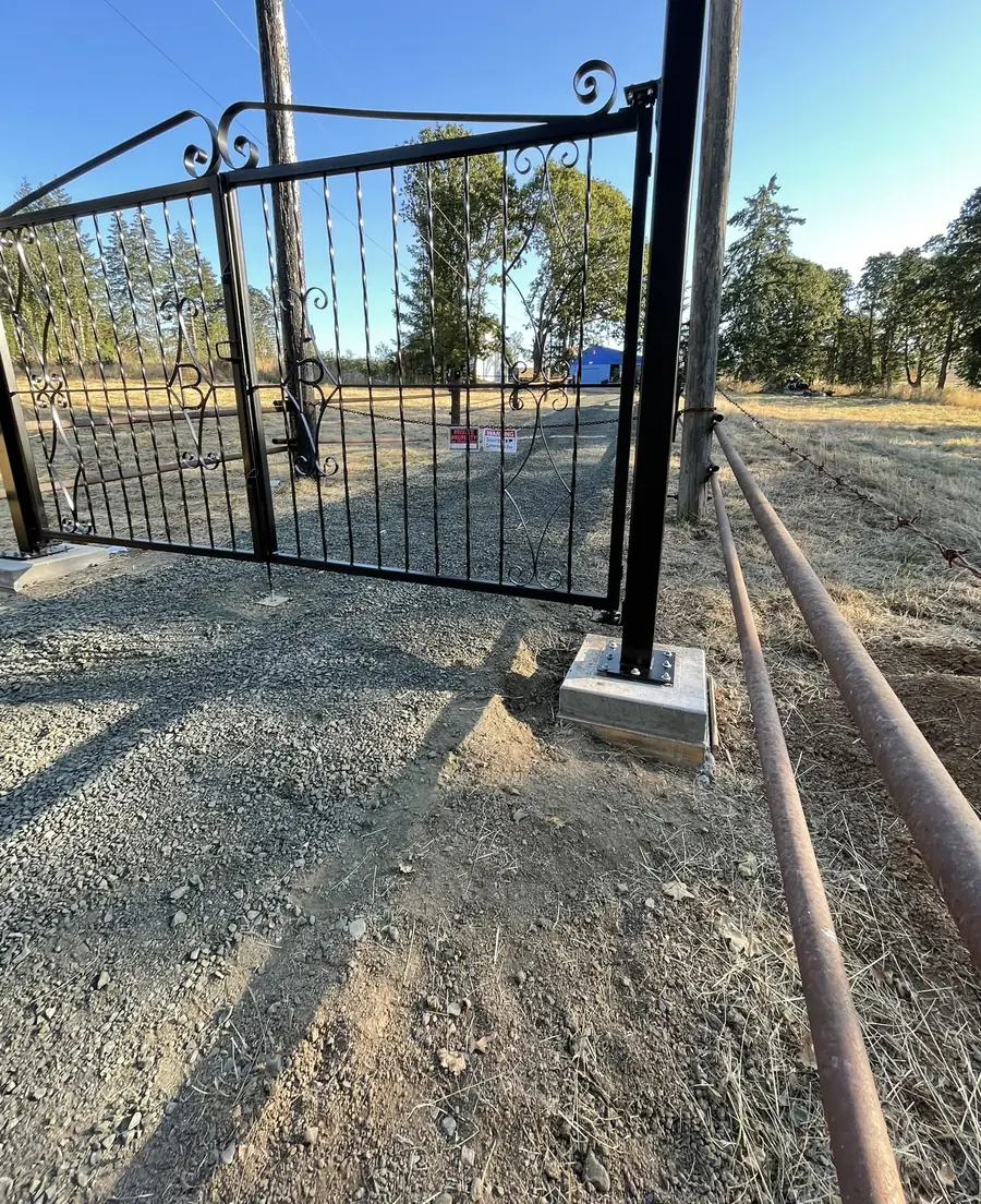 Steel gate with scrollwork on square posts set in concrete at a farm driveway