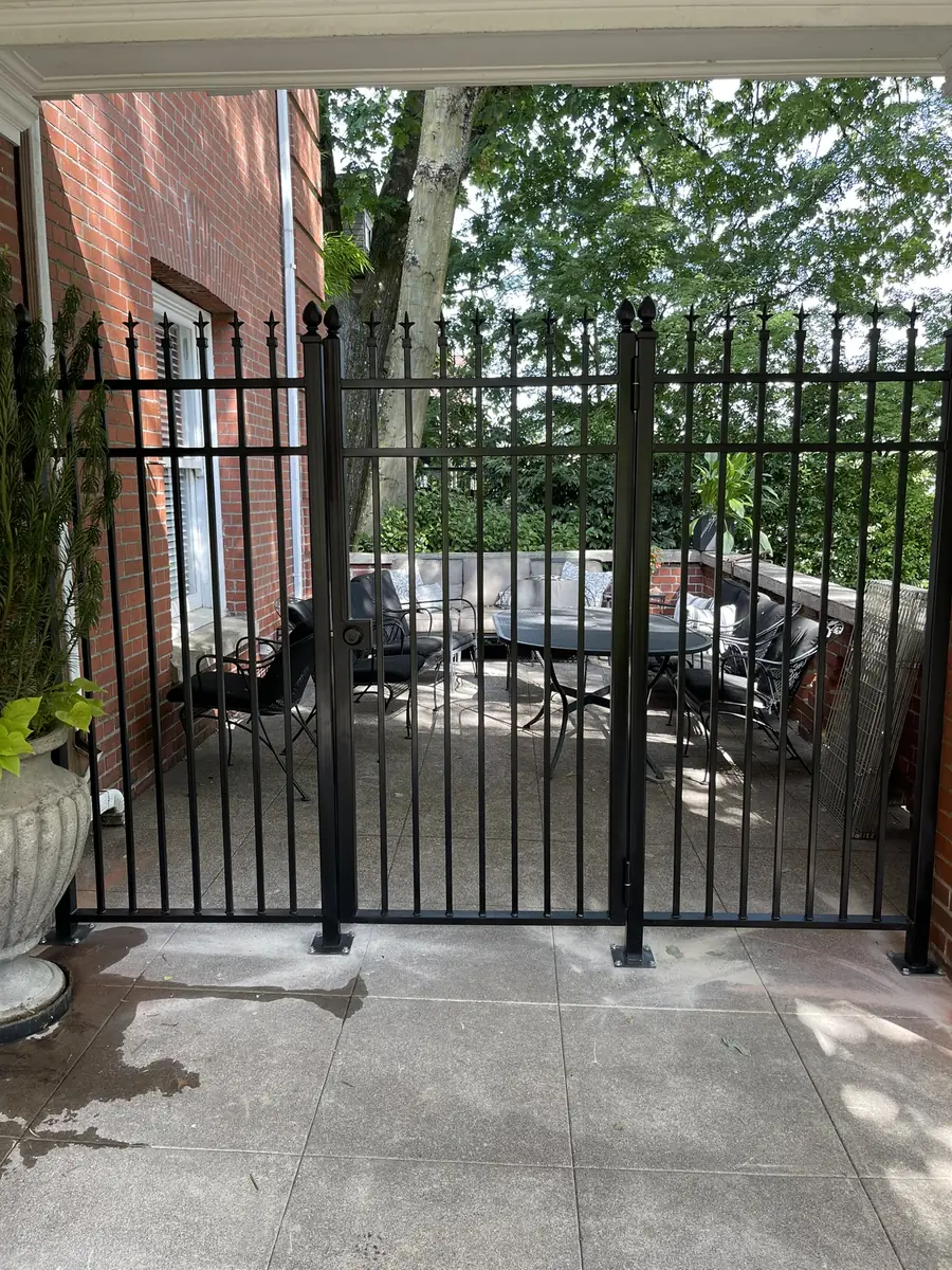 Black iron fence and gate closing in a patio beside a brick house