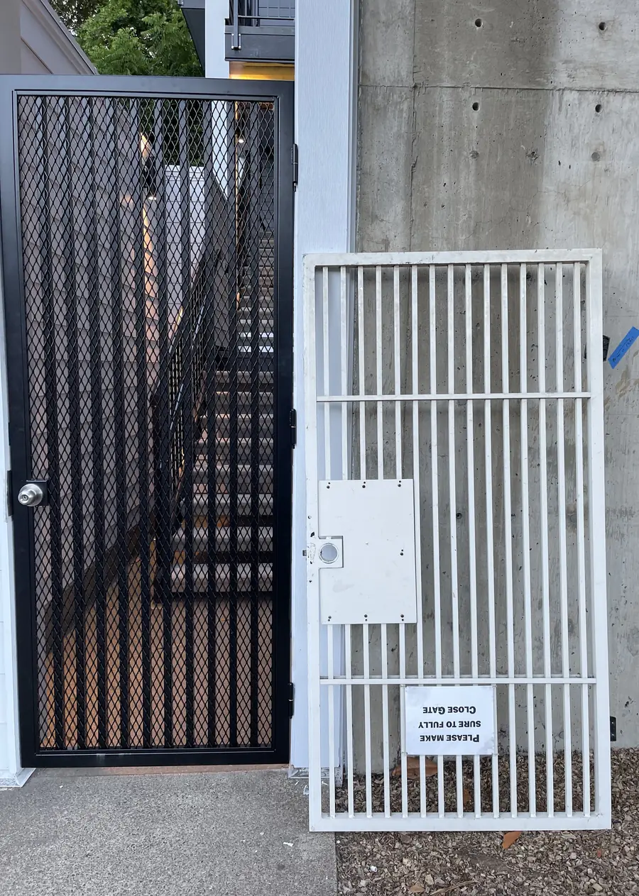 Old white bar security gate leaning next to the new black mesh gate that replaced it
