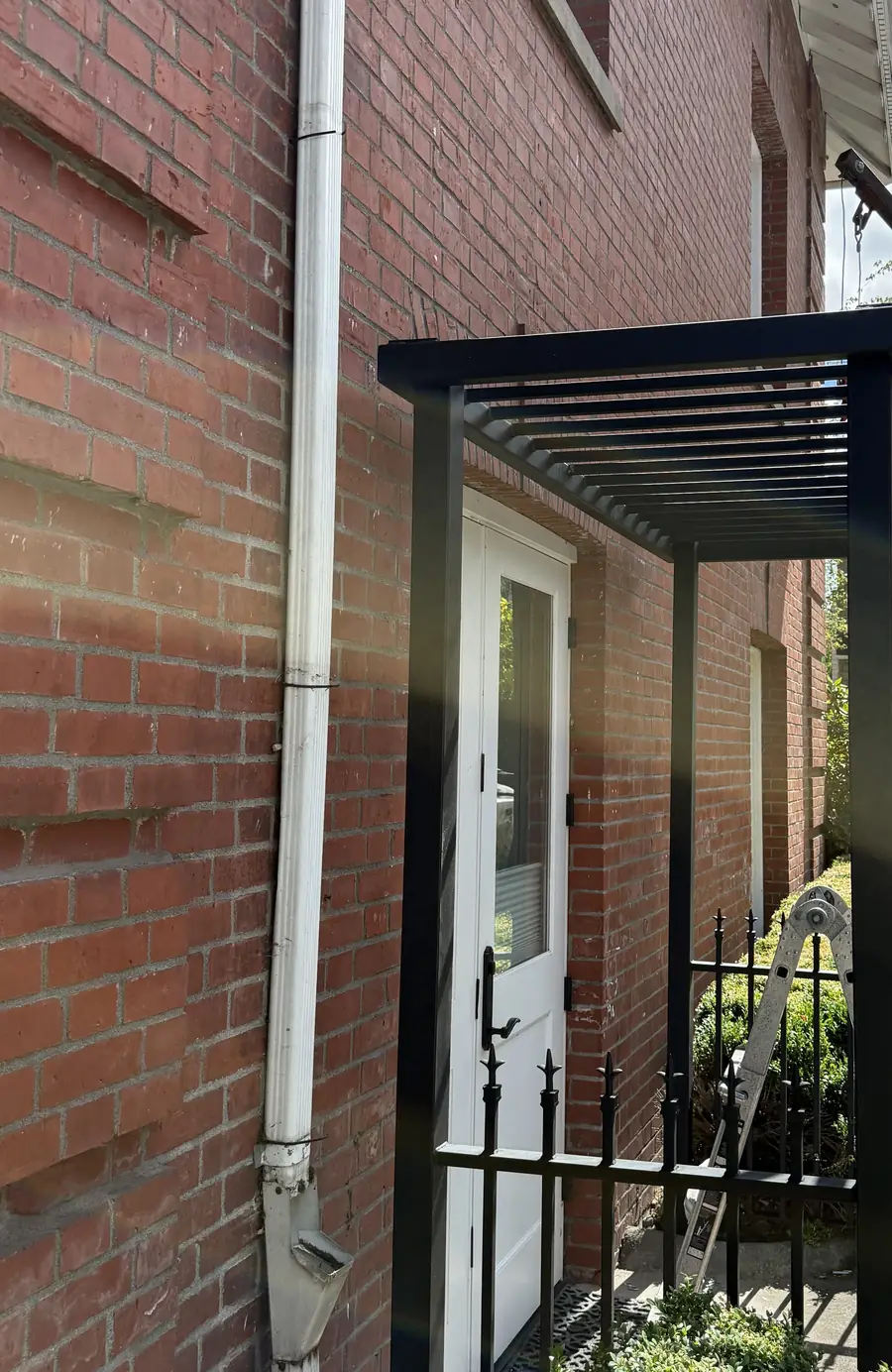 Black steel entry canopy seen from the side along a brick wall